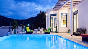 A modern pool area with clear blue water, lounge chairs, and a well-lit outdoor space. - Zidanos Luxurious Villa (Lefkada)