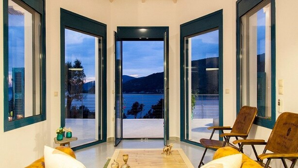 A room with a sofa, chairs, and a view of a lake and mountains through large windows. - Zidanos Luxurious Villa (Lefkada)