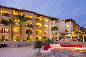 A multi-story hotel with a courtyard featuring a stone seating area and palm trees.