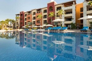 A hotel with a swimming pool, multiple balconies, and palm trees.