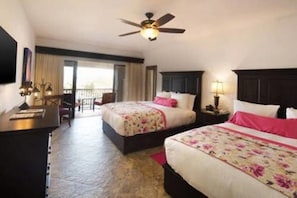 A hotel room with two beds, a desk, a ceiling fan, and a balcony with a view.