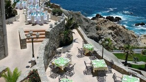 A coastal outdoor dining area with tables and chairs arranged on a stone terrace overlooking the ocean. - Rated for the Best Value in Cabo San Lucas!! 2BR 8P (Cabo San Lucas)