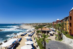 Un resort con vista a la playa, sillas de descanso, sombrillas y zona de piscina.