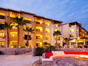 Un hotel con varios balcones, palmeras y una zona circular de estar con una chimenea.