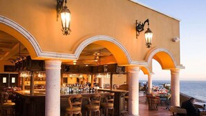 An outdoor bar area with multiple seating arrangements, including bar stools and chairs, under a structure with arches. - Unique Master 1 Bedroom Suite 1 King (Cabo San Lucas)