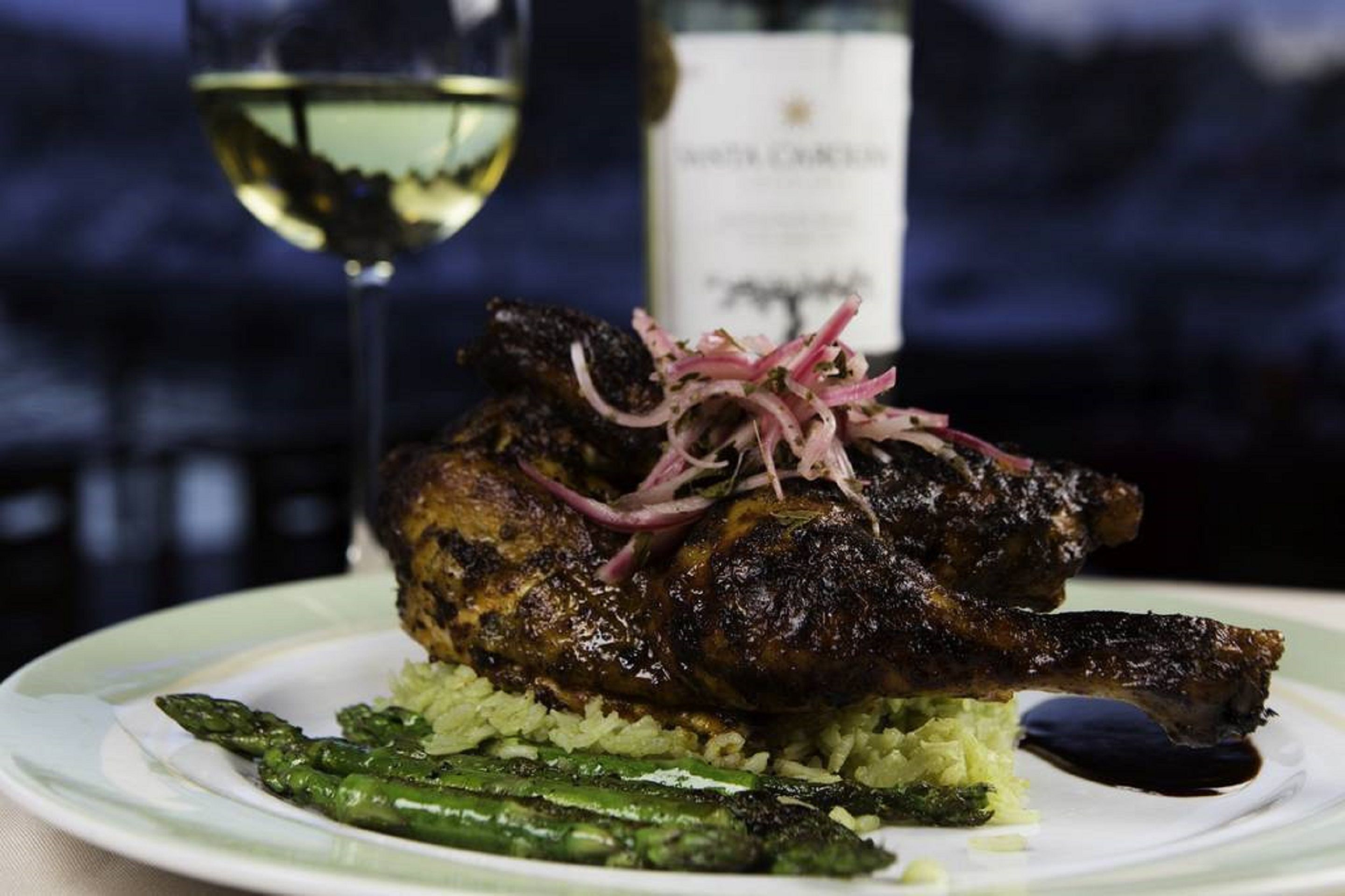 A plate with roasted meat, asparagus, and a bottle of wine in the background.