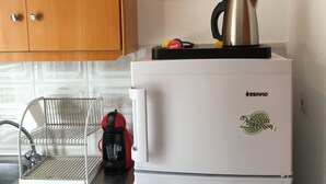 Una kitchenette con un refrigerador blanco, una cafetera y un hervidor.