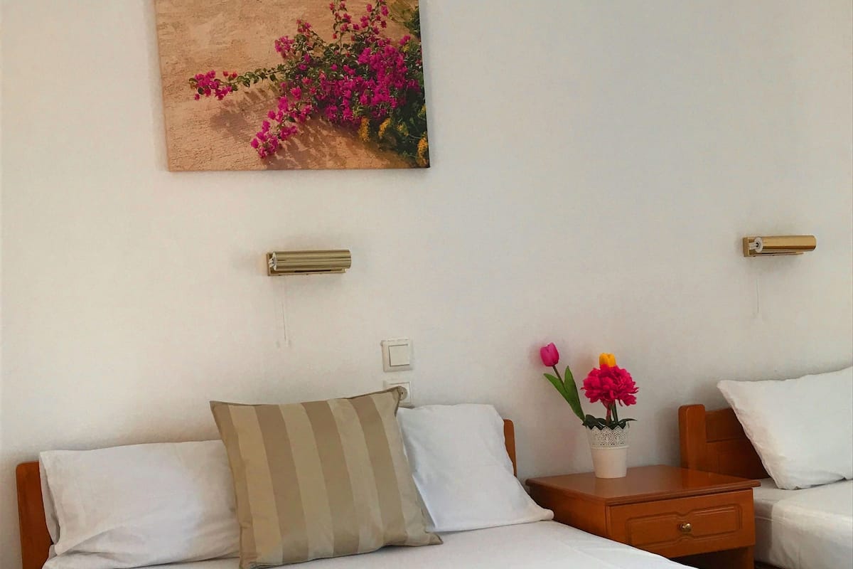 Ein Hotelzimmer mit einem großen Bett, zwei Nachttischen, einem Wandgerät zur Klimatisierung und einem Blumenbild.