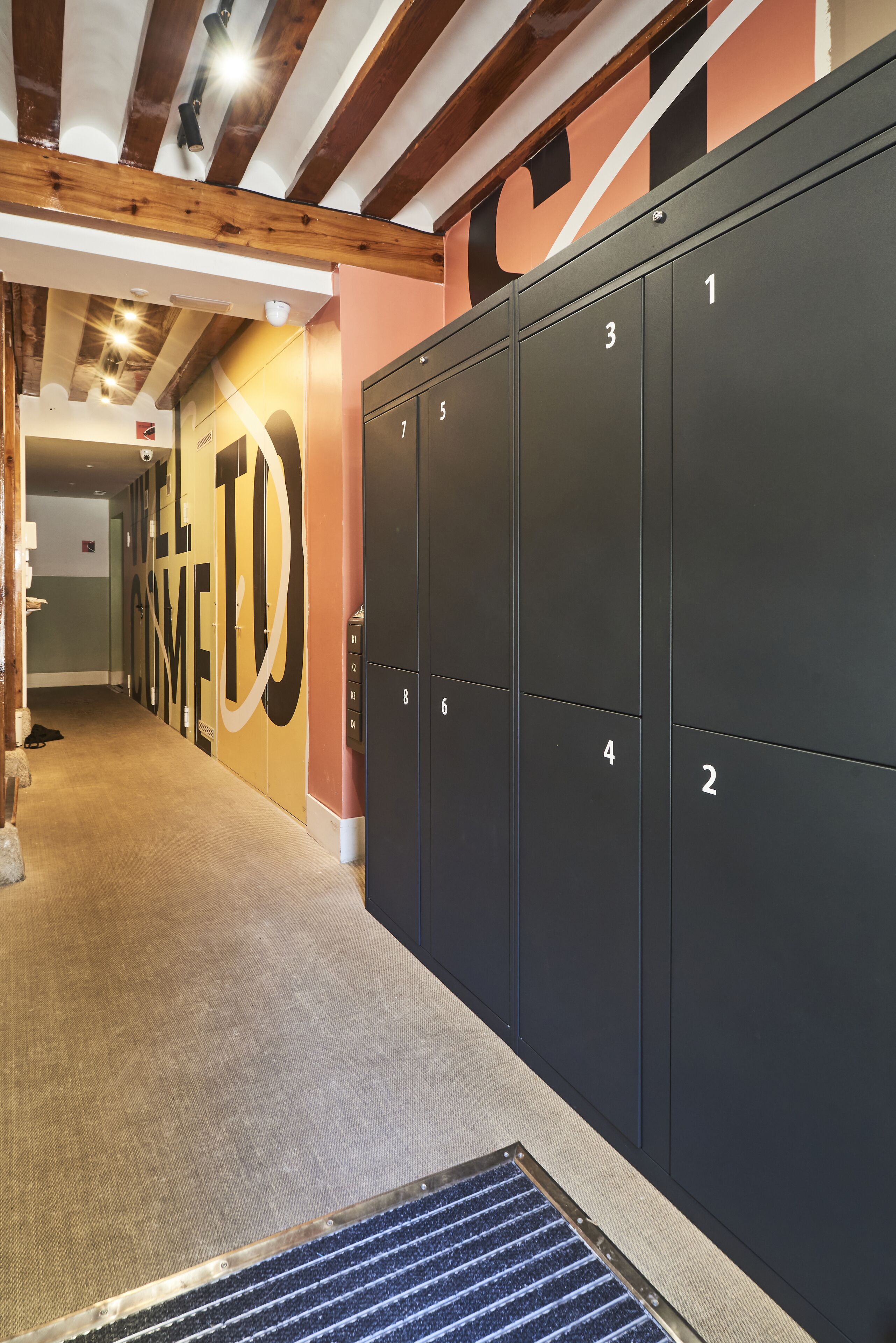 A hallway with lockers numbered 1 to 8, a carpeted floor, and a 'WELCOME' sign on the wall.