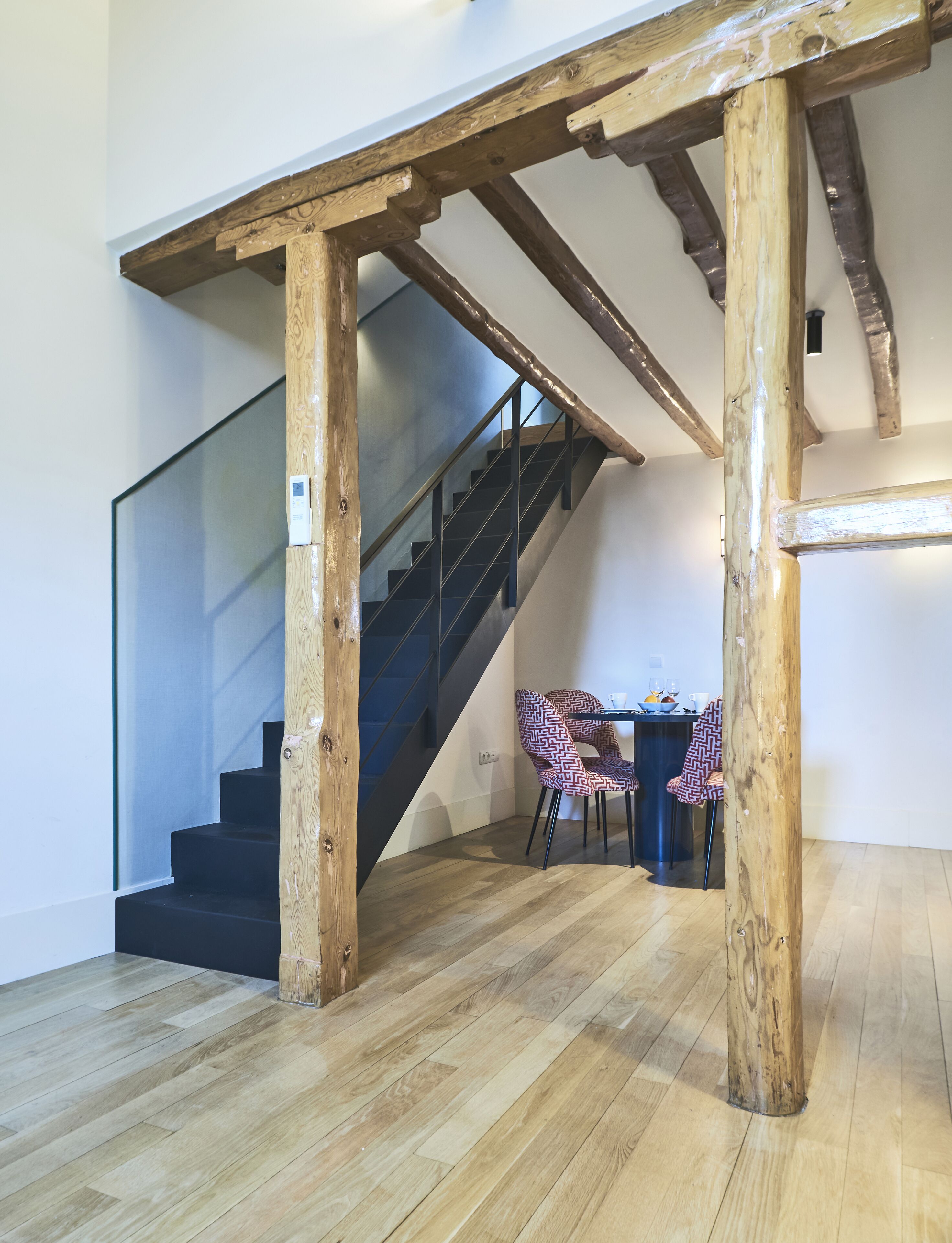 Eine Treppe mit Holzbalken, ein Essbereich mit Tisch und Stühlen sowie ein Blick auf das Obergeschoss.