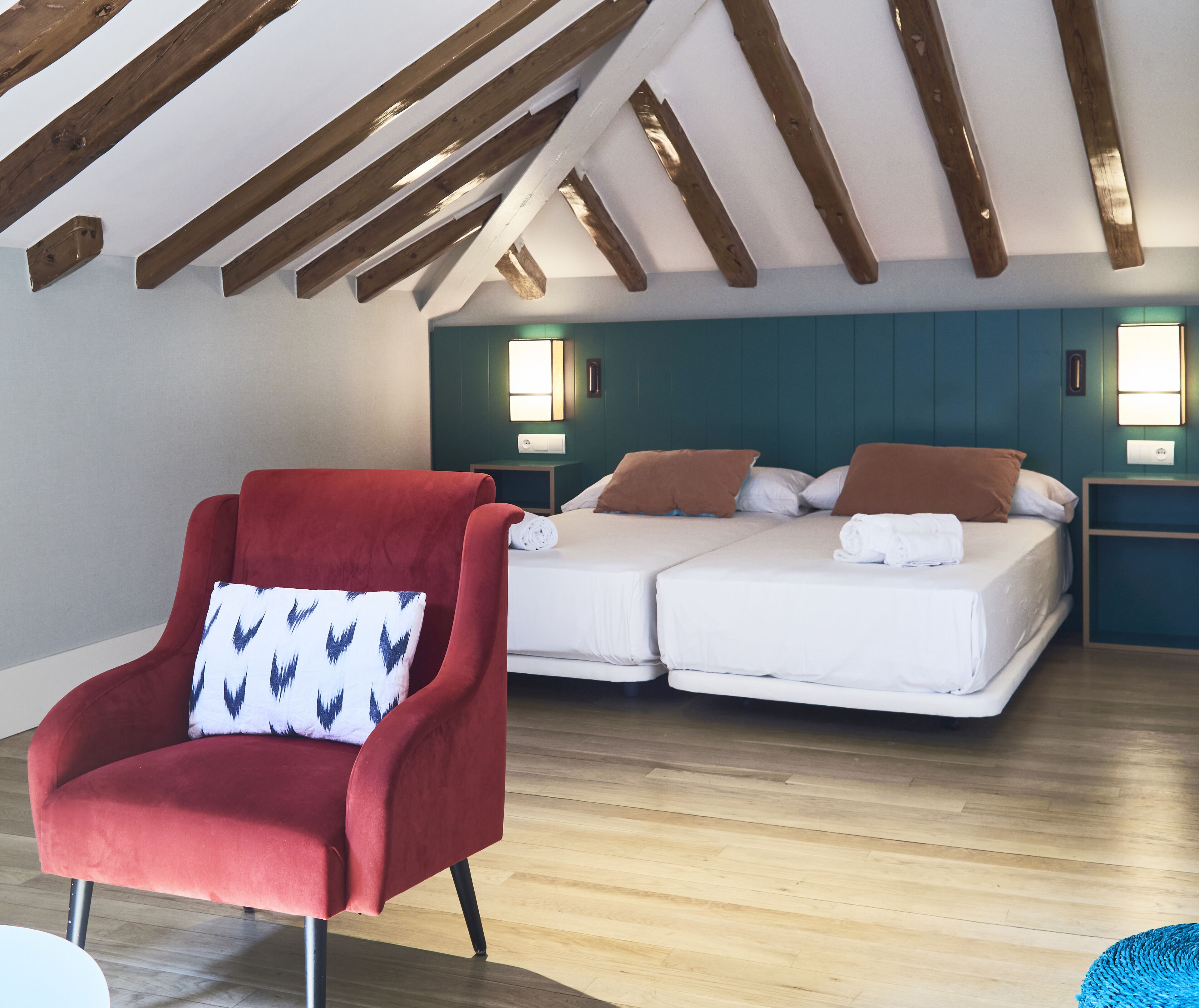 A room with a red armchair, a bed with white bedding, wooden beams on the ceiling, and green walls.