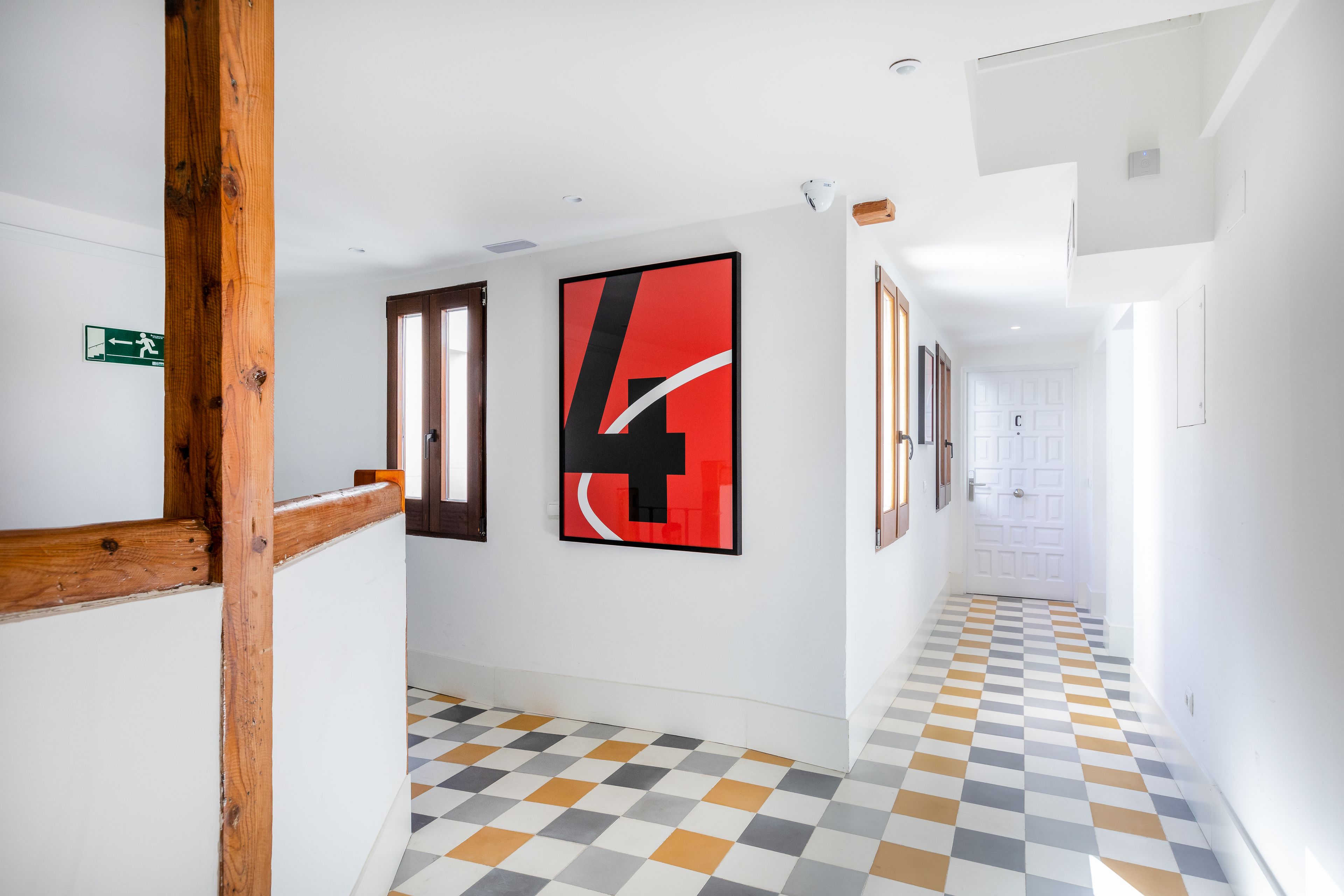 A hallway with a checkered floor, wooden beams, and a large red and black artwork on the wall.