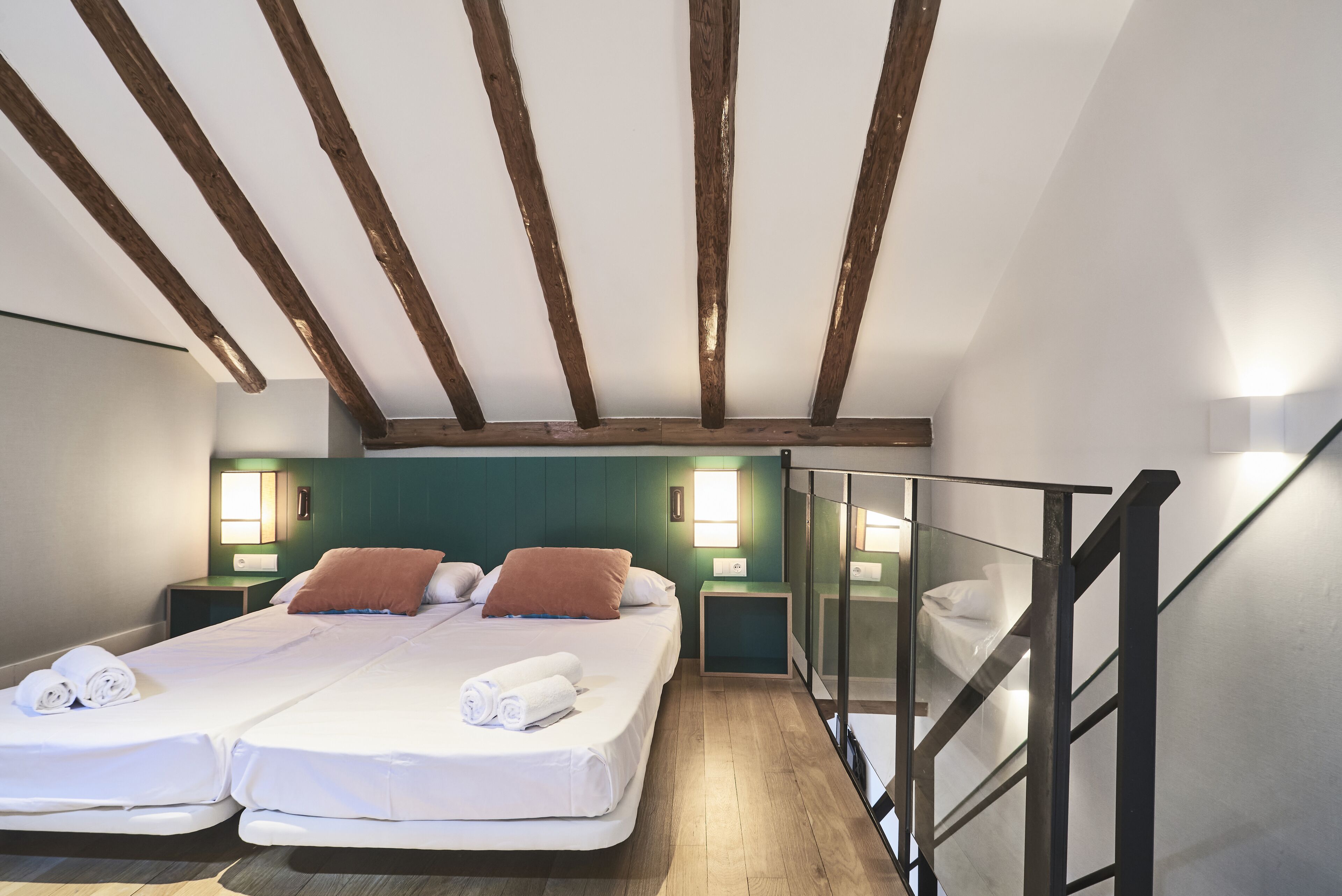 A room with two beds, wooden beams on the ceiling, and two bedside tables with lamps.