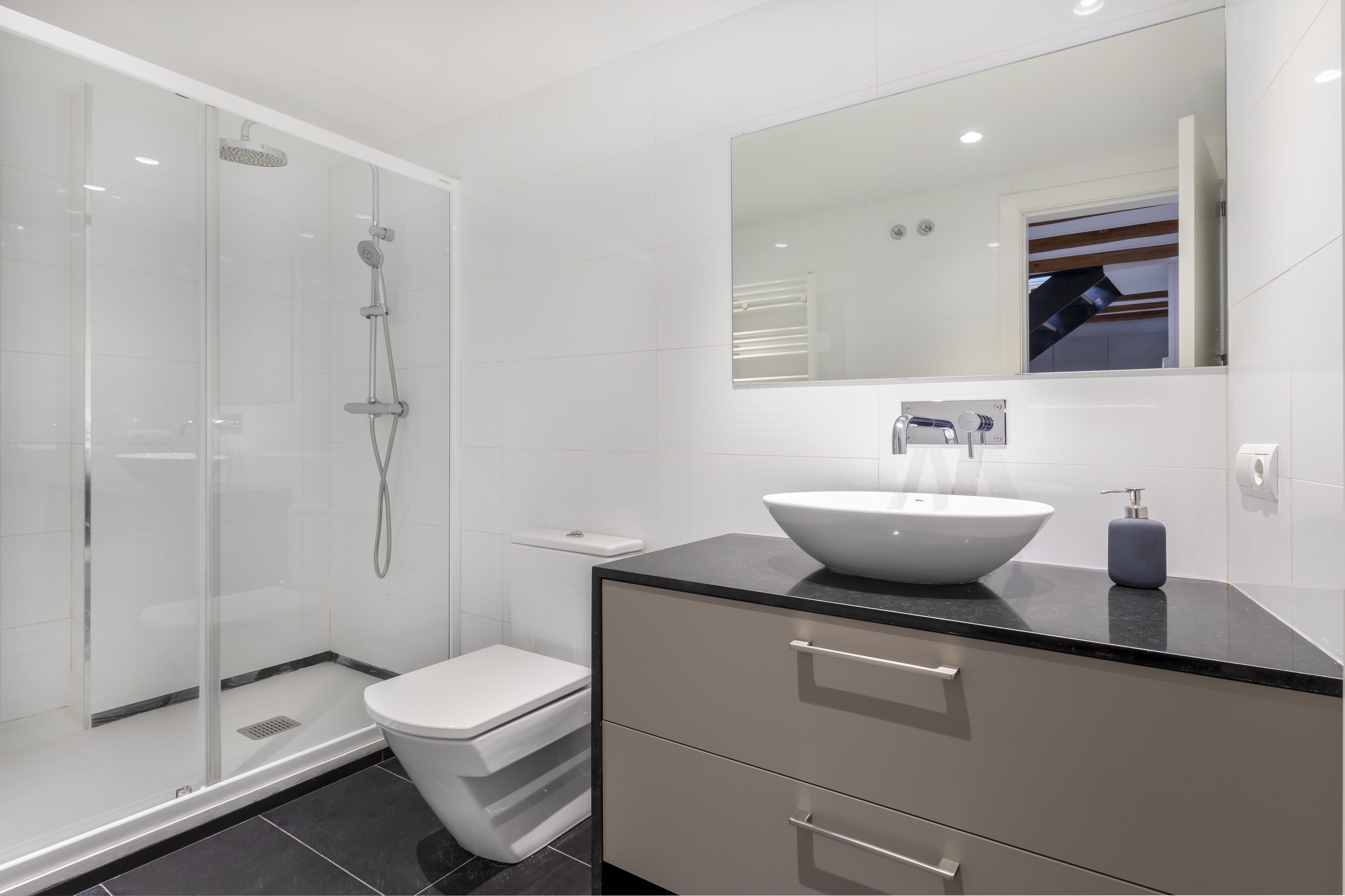 A modern bathroom with a glass-enclosed shower, a white toilet, a large mirror, and a black countertop with a white sink.