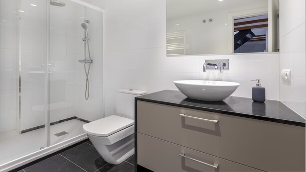 Une salle de bain moderne avec une douche à parois de verre, des toilettes blanches, un grand miroir et un plan de toilette noir avec un lavabo blanc.