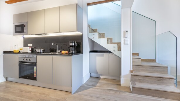 Una cocina moderna con horno empotrado, microondas y cafetera, y una escalera que sube a un nivel superior.