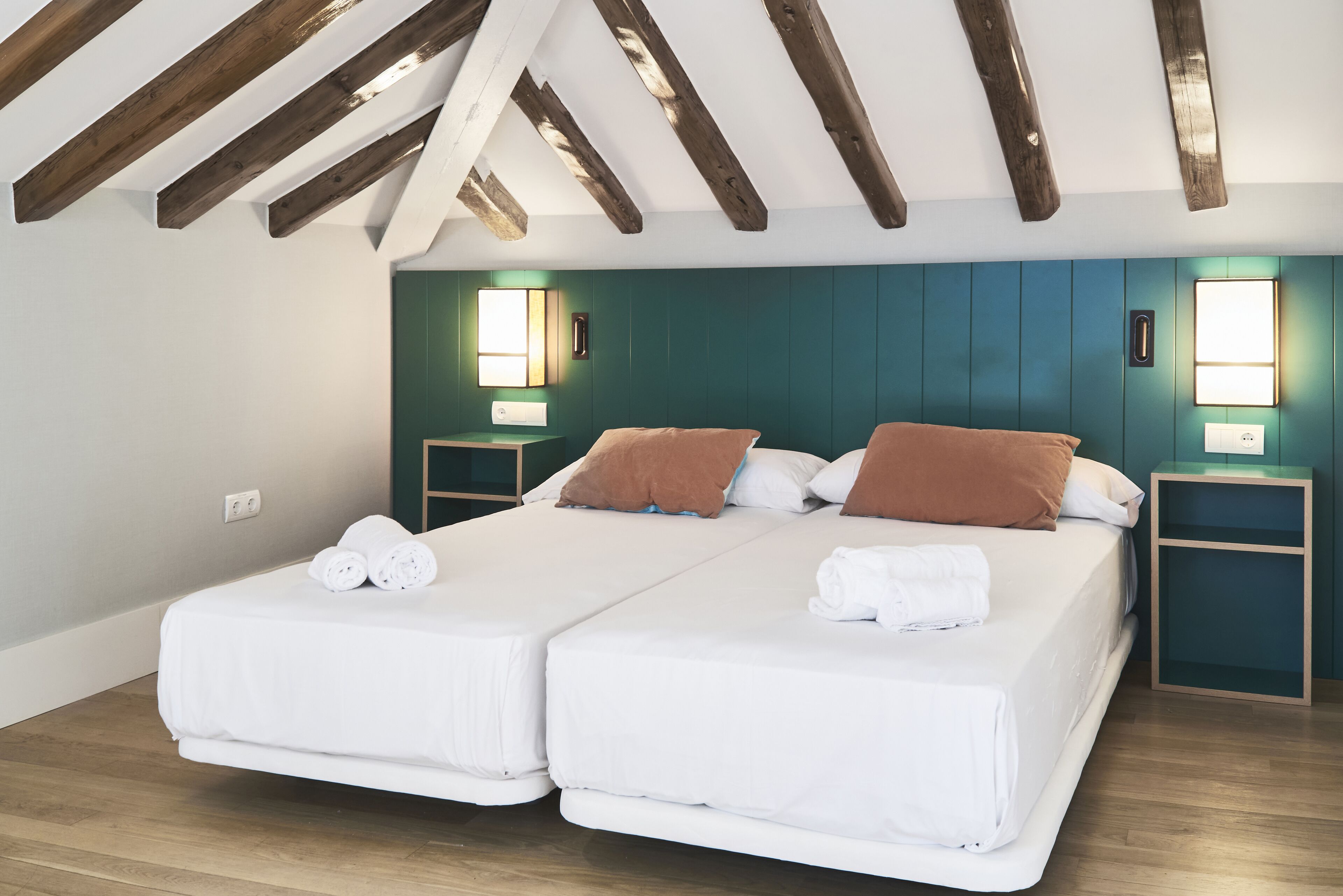 A double bed with white linens and brown pillows in a room with wooden beams on the ceiling and teal walls.