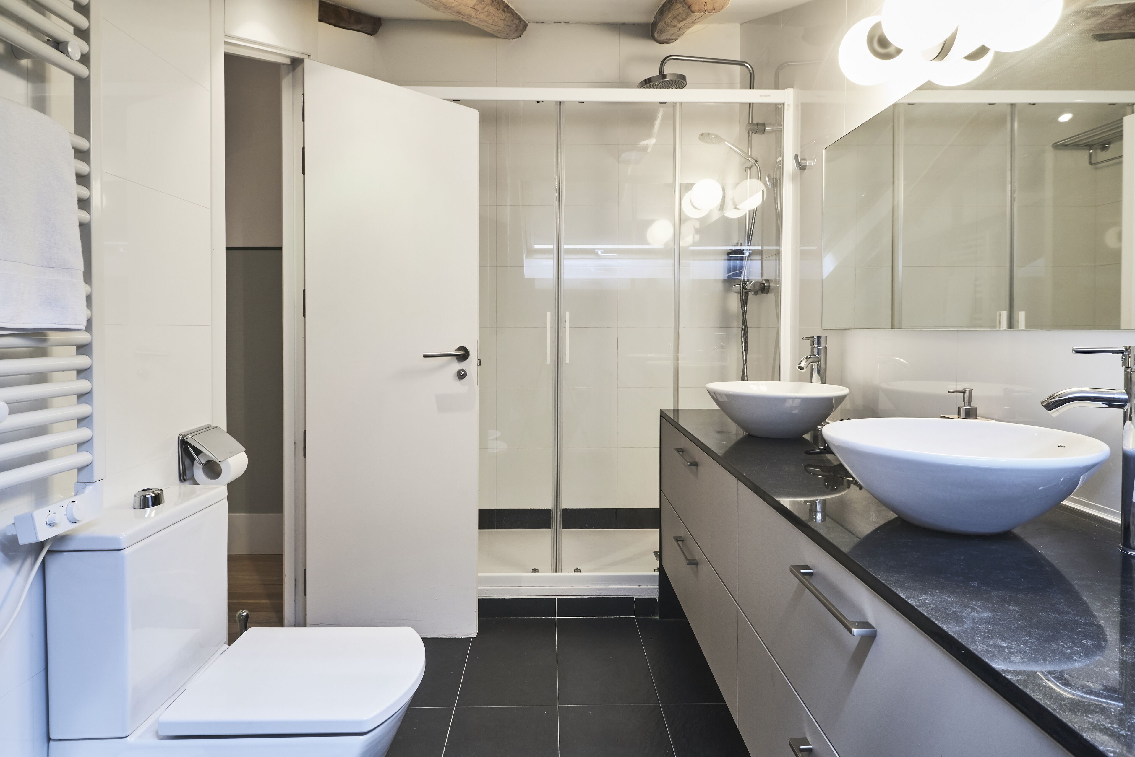 A modern bathroom with a glass-enclosed shower, two sinks, a toilet, and a built-in washing machine.