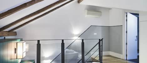 Ein Schlafzimmer mit schrägen Wänden, einer Glasstufen-Treppe, einem Bett mit weißer Bettwäsche und Holzboden.