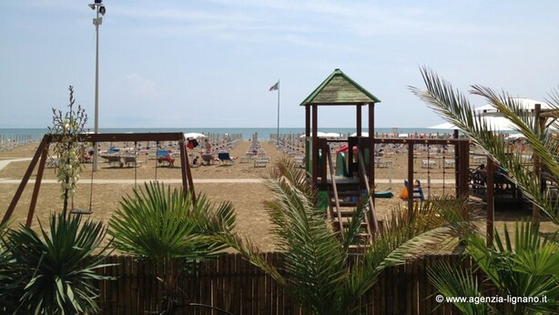Ein Strand mit einer hölzernen Konstruktion, möglicherweise einem Pavillon, und einer Fahnenstange.