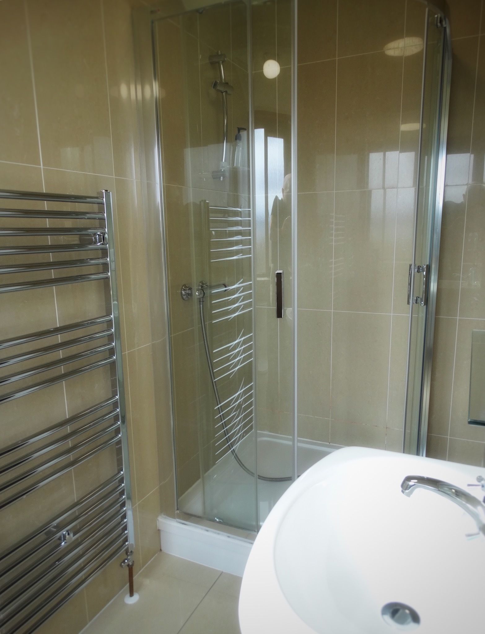 A modern bathroom with a glass-enclosed shower, a chrome towel rack, and a white sink.