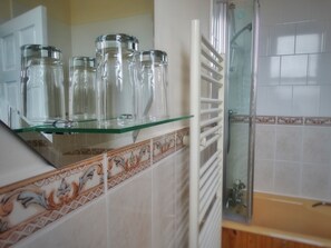 A bathroom with a glass shelf holding clear glass jars, a white towel rack, and a shower area with a glass door. - Kilchoan House Hotel (Acharacle)