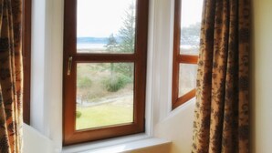 A room with a bay window featuring a view of a grassy area and trees. - Kilchoan House Hotel (Acharacle)