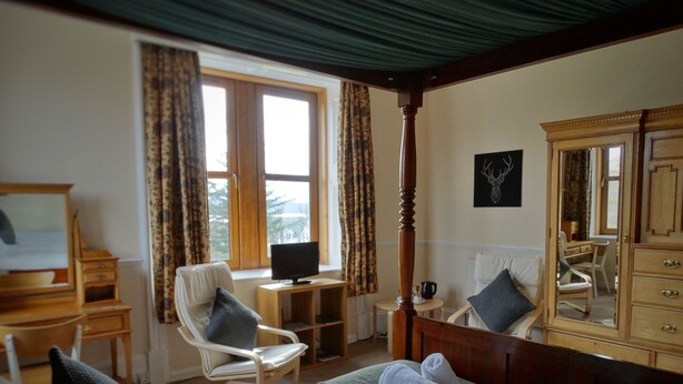 A hotel room with a bed, a desk, a chair, a television, a dresser, and a large mirror. - Kilchoan House Hotel (Acharacle)