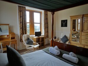 A hotel room with a bed, a desk, a chair, a television, a dresser, and a large mirror. - Kilchoan House Hotel (Acharacle)