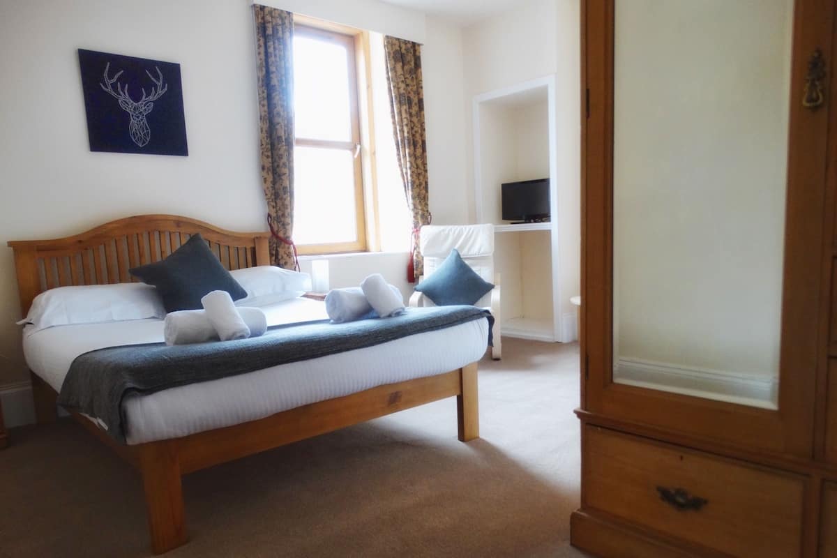 A bedroom with a wooden bed, white bedding, and a blue and white patterned throw.