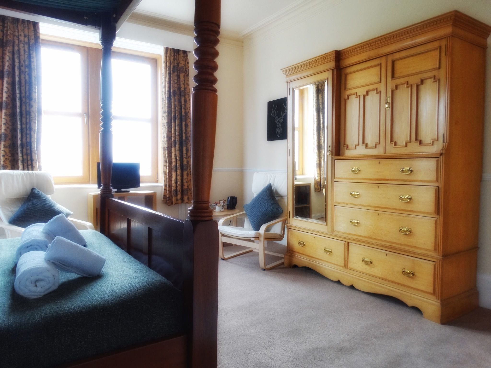 A bedroom with a four-poster bed, a wooden dresser with multiple drawers, a chair, and a television on a small table.