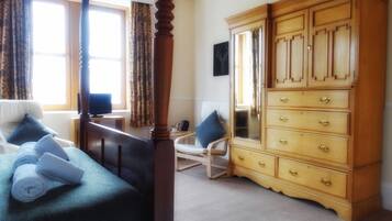 A bedroom with a four-poster bed, a wooden dresser with multiple drawers, a chair, and a television on a small table.