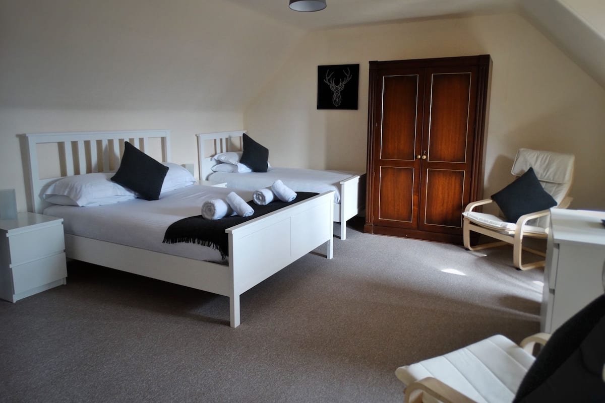 A bedroom with two beds, a wardrobe, a chair, and a desk.