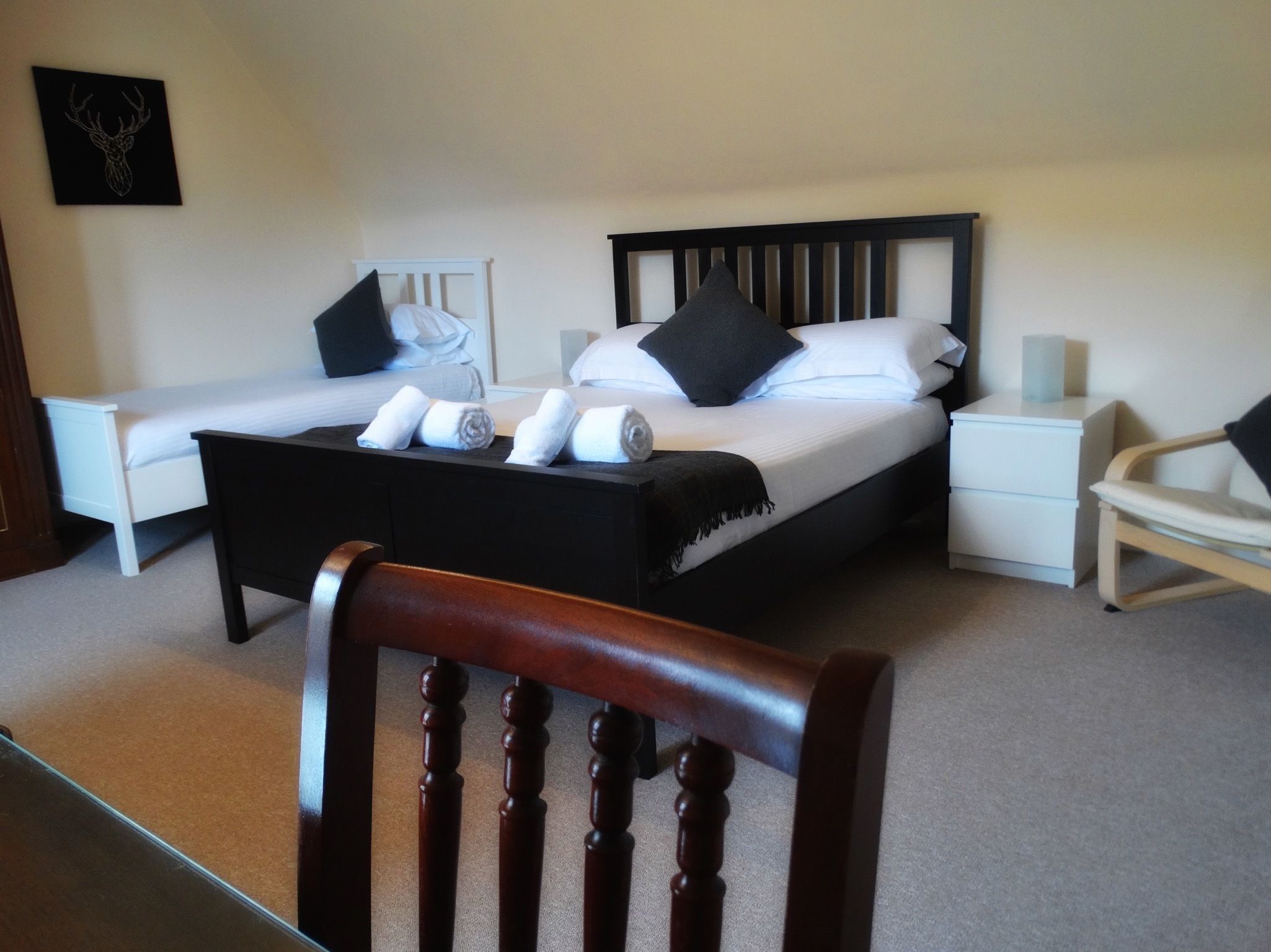 A bedroom with a double bed, a smaller bed, a bedside table, a chair, and a wall-mounted artwork.