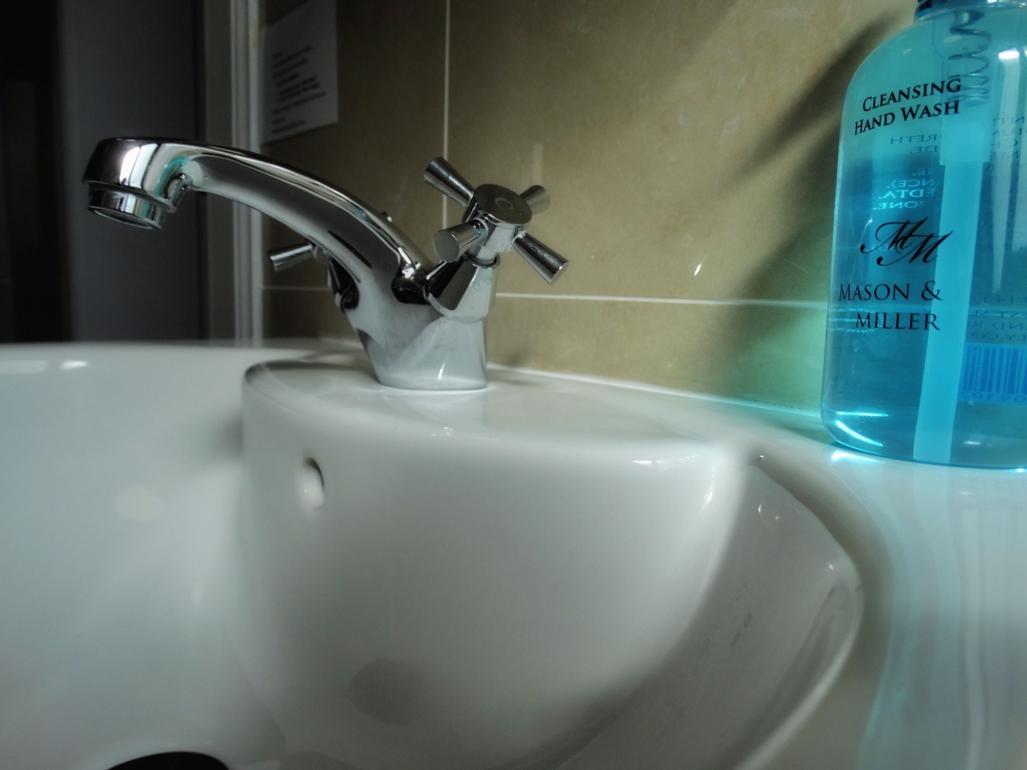 A bathroom sink with a chrome faucet and a bottle of hand wash soap.