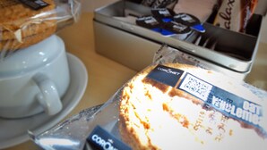 A breakfast setup with a coffee cup, a packaged cake, and a container with snacks. - Kilchoan House Hotel (Acharacle)