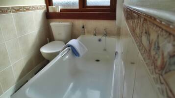 A bathroom with a bathtub, toilet, and window.