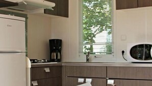 Une cuisine moderne équipée d’un réfrigérateur, d’un four à micro-ondes et d’une cuisinière. Sur la table, on trouve deux bols rouges et blancs à pois.