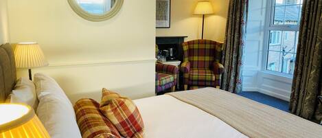 A hotel room with a bed, two lamps, a chair, a desk with a coffee maker, a mirror, and a window with curtains.