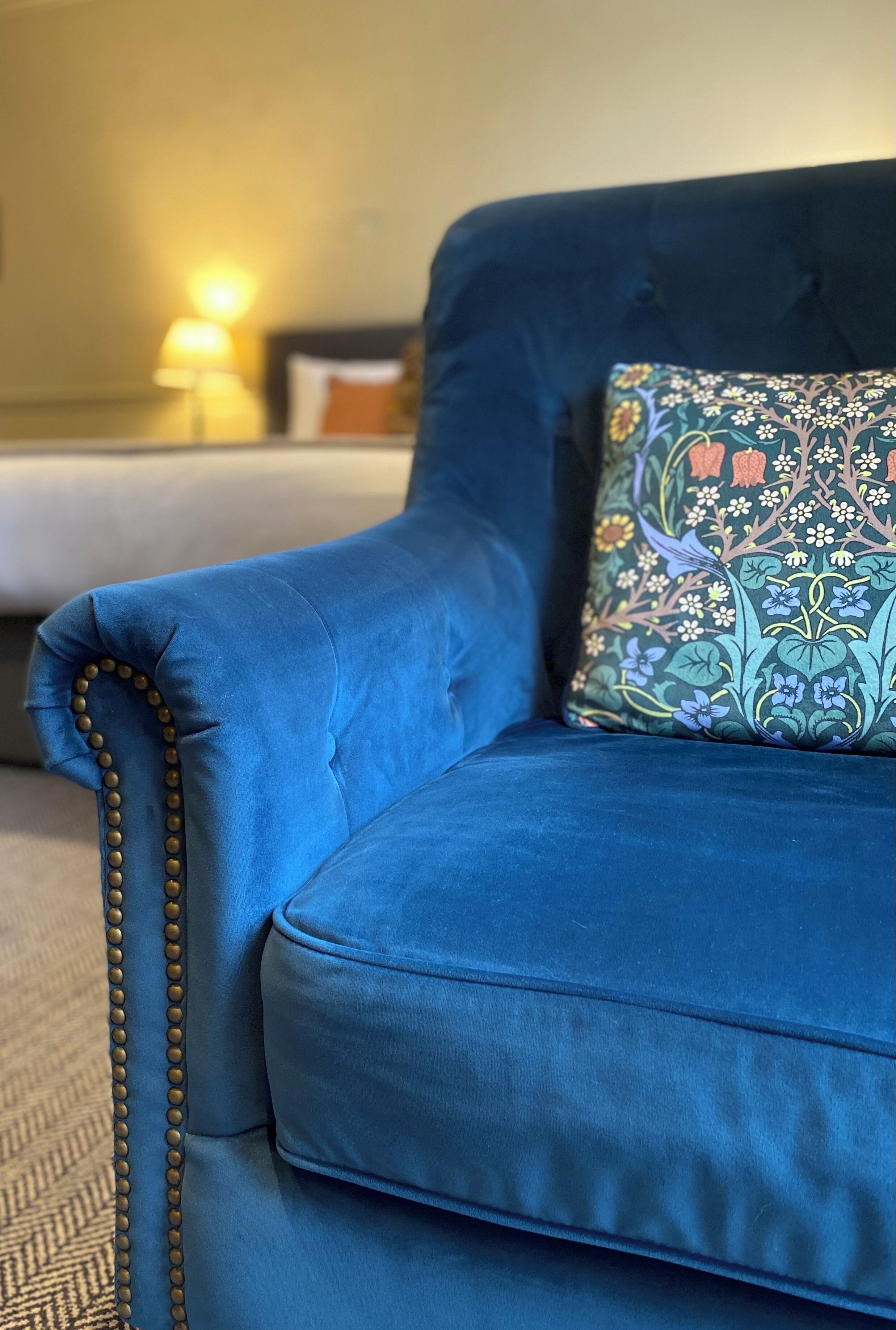 Un canapé bleu avec un coussin à motifs floraux et une bordure ornée de perles.