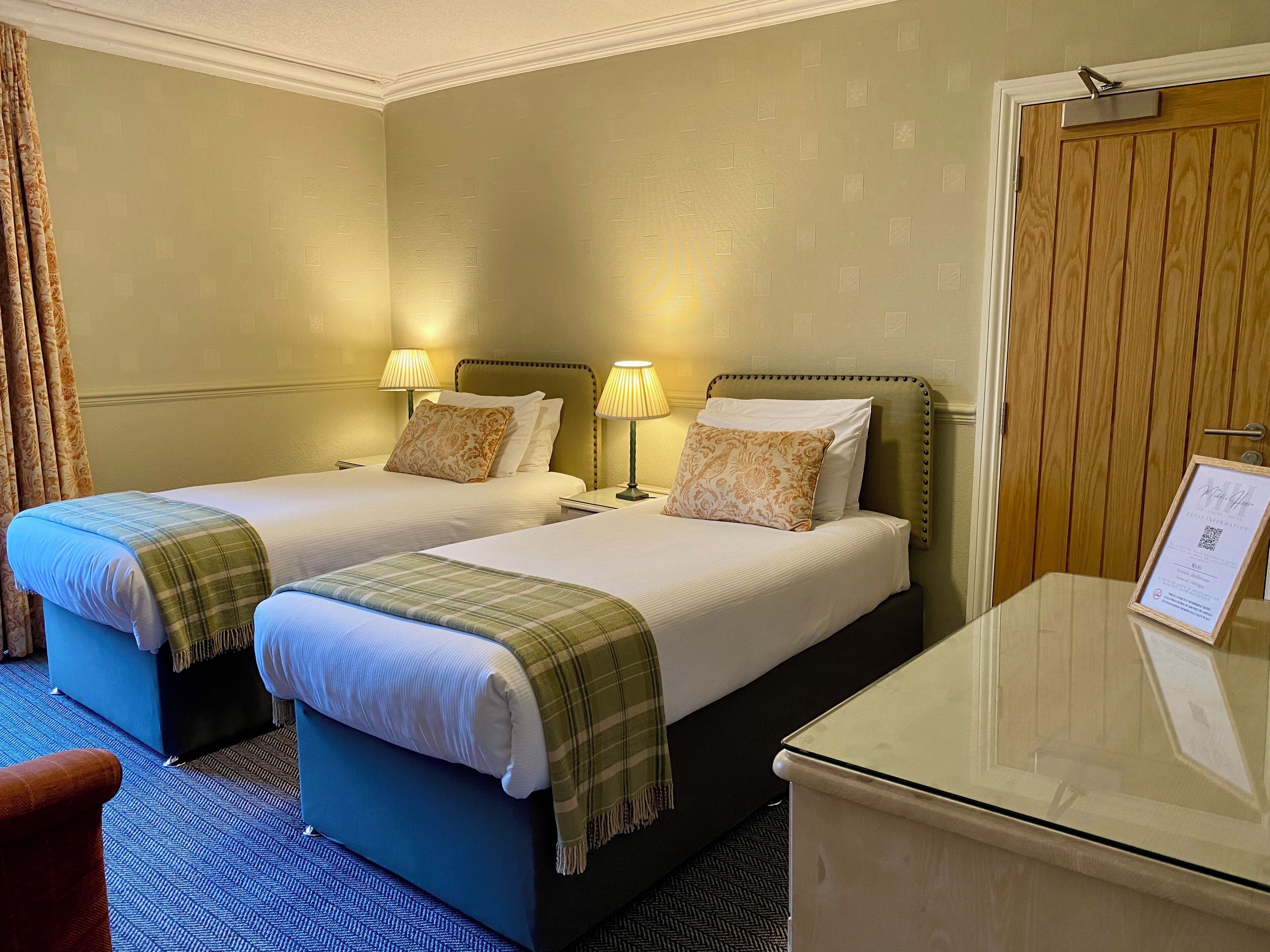 A hotel room with two beds, a desk, and a door.