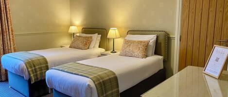 A hotel room with two beds, a desk, and a door.