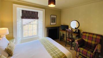 A hotel room with a bed, a television, a fireplace, a chair, and a window with a view of a brick building.
