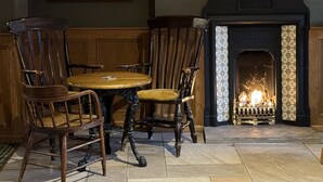 A cozy room with a fireplace, wooden chairs, a round table, and a framed landscape painting on the wall. - Middle House (Leyburn)