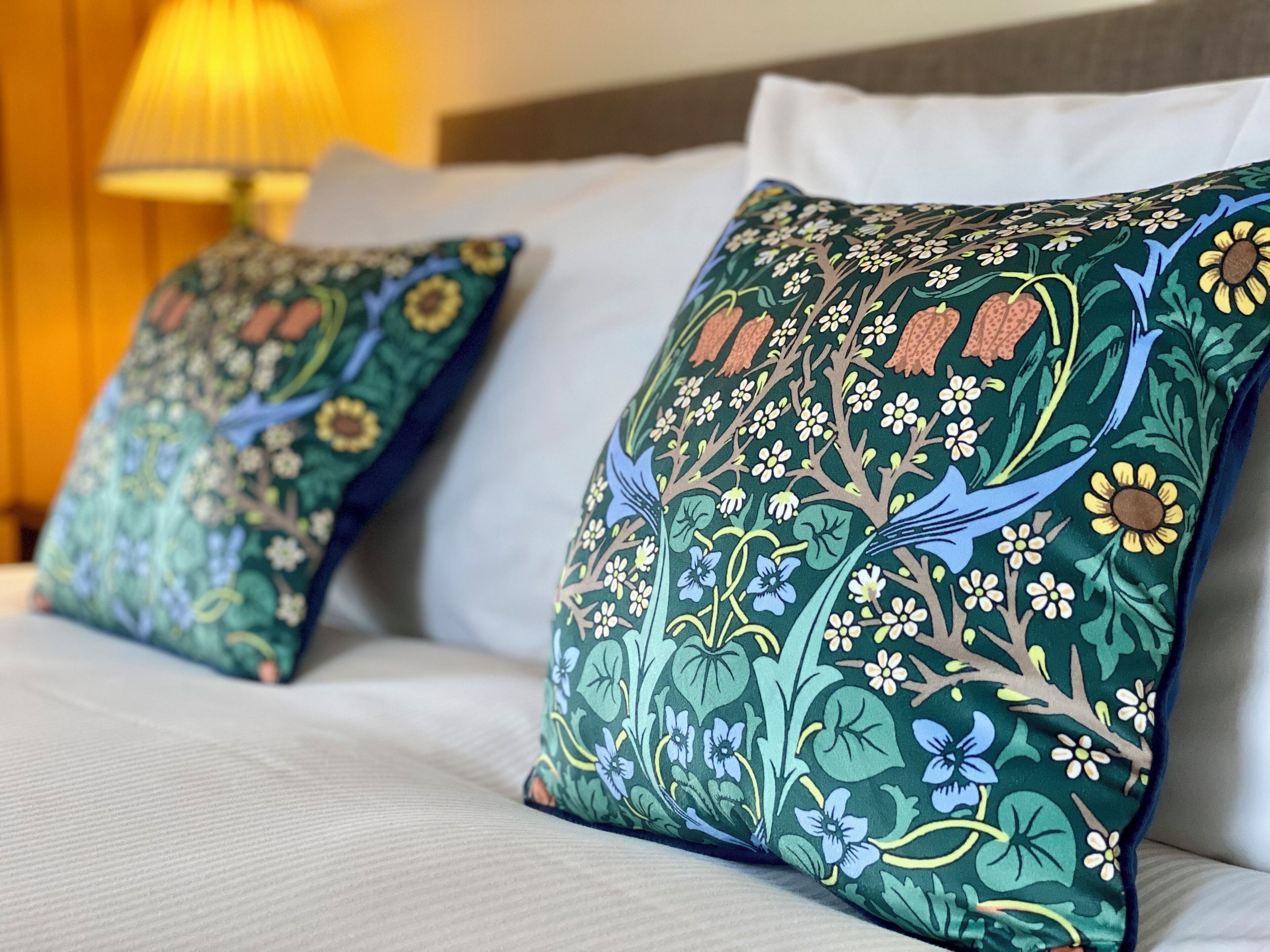 Una cama con dos almohadones decorativos con motivos florales y de pájaros.