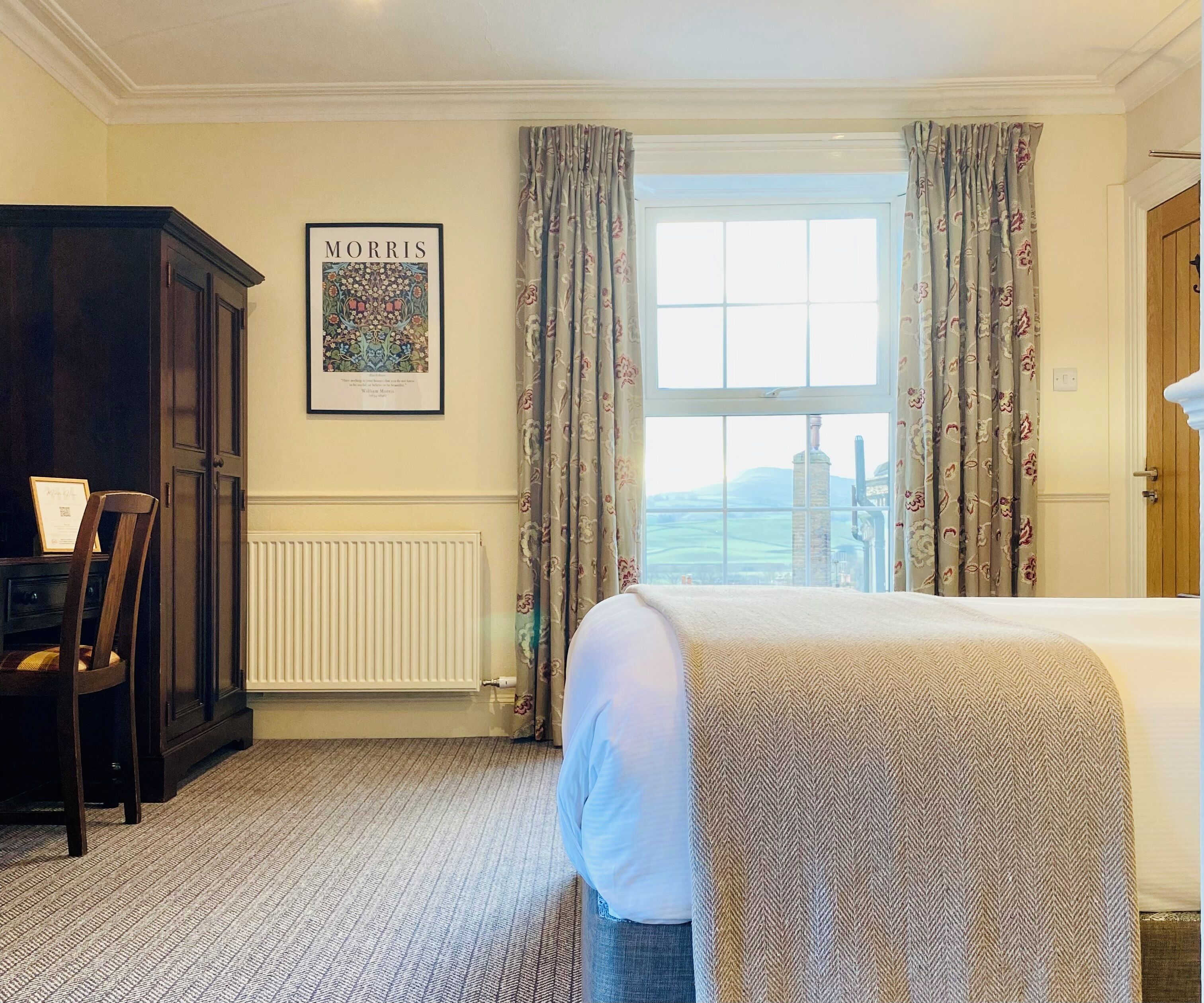 A hotel room with a bed, a radiator, a framed picture on the wall, and a view through the window.