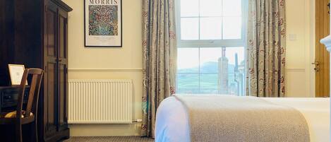 A hotel room with a bed, a radiator, a framed picture on the wall, and a view through the window.