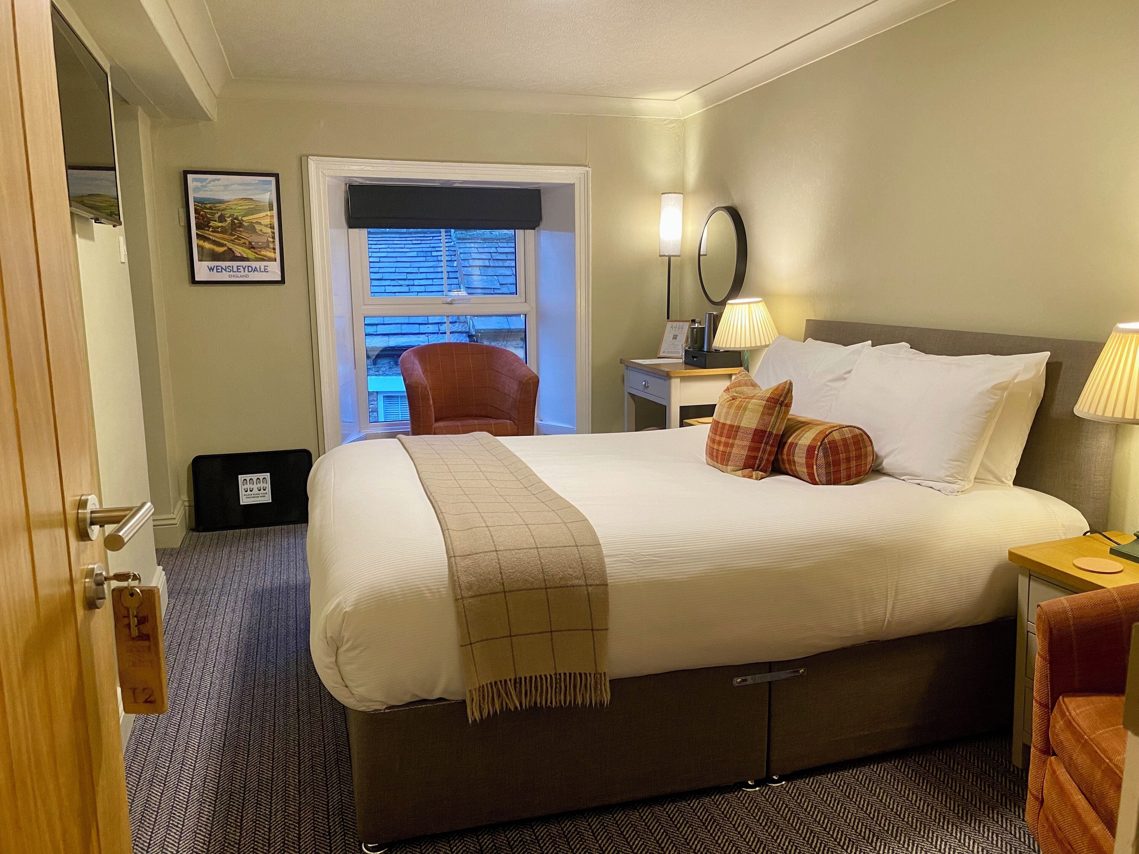 A hotel room with a large bed, a chair, a desk, and a window with blinds.