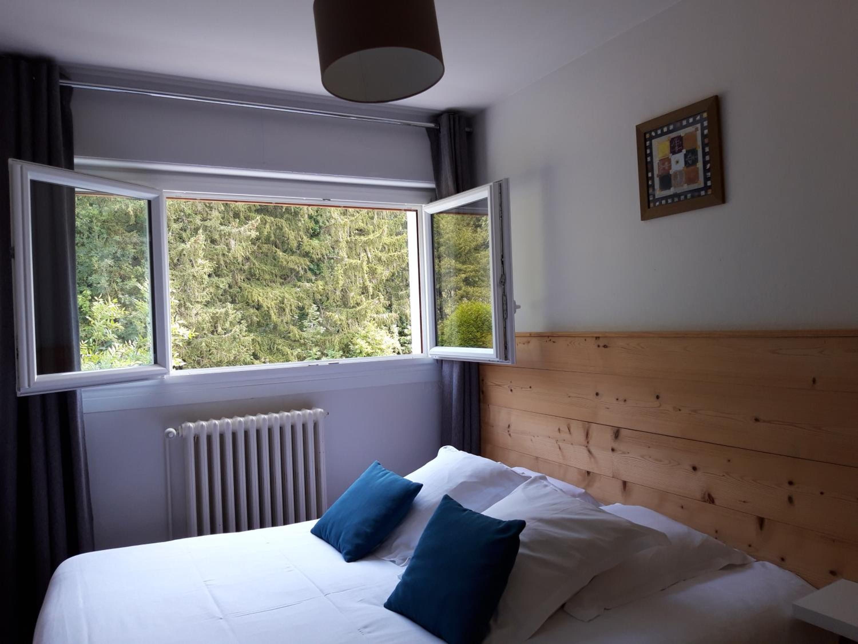 Un dormitorio con cama, ventana con vistas a árboles, radiador y cabecero de madera.