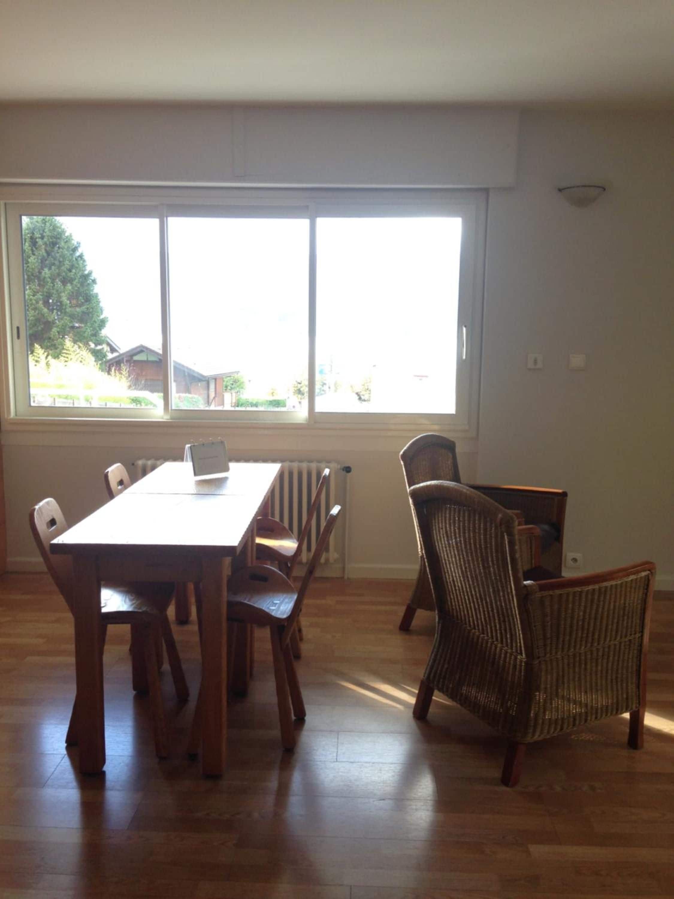 A dining area with a wooden table and chairs, large windows, and a view of the outdoors.